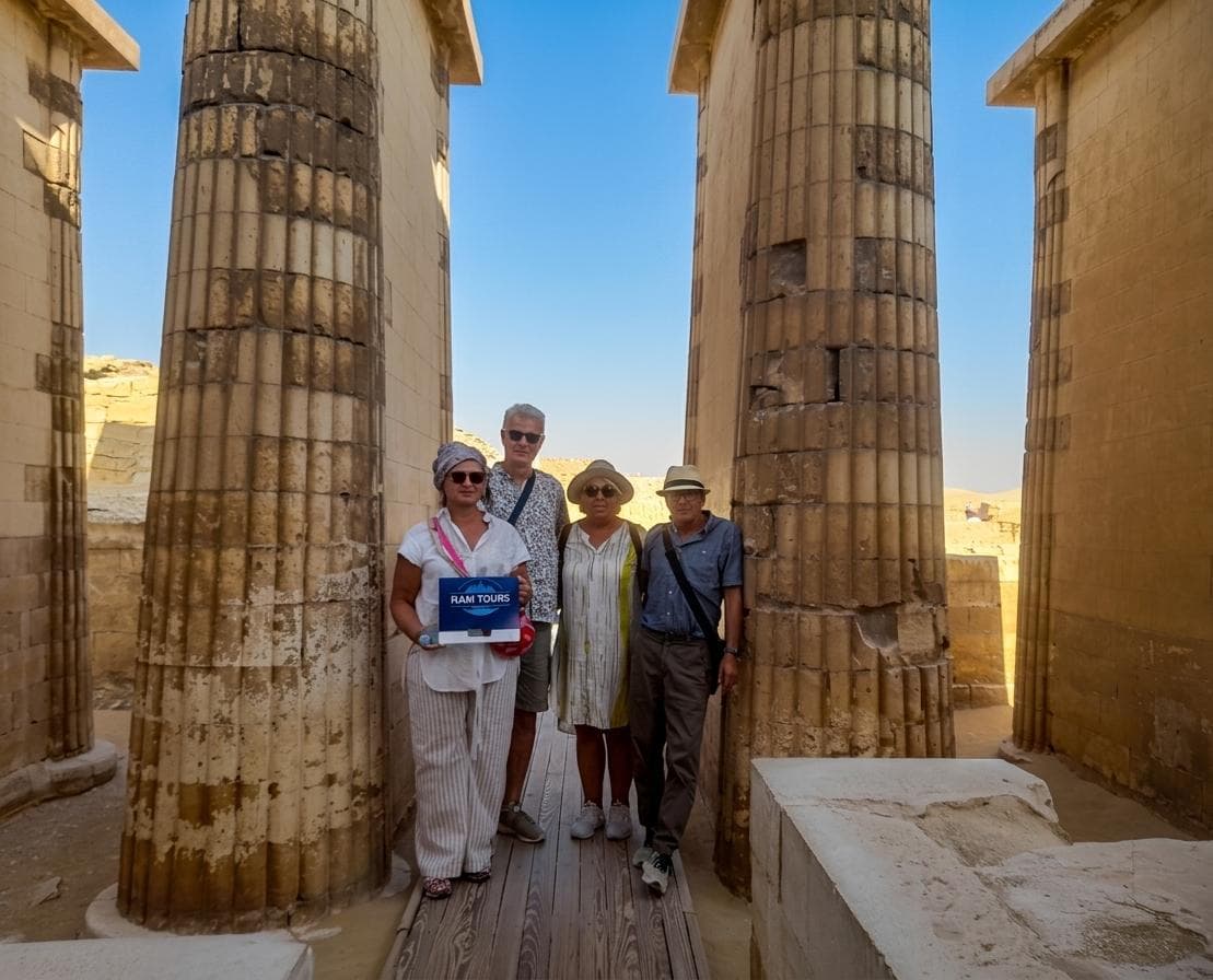 Four tourists pose between massive fluted stone columns at an ancient Egyptian archaeological site.