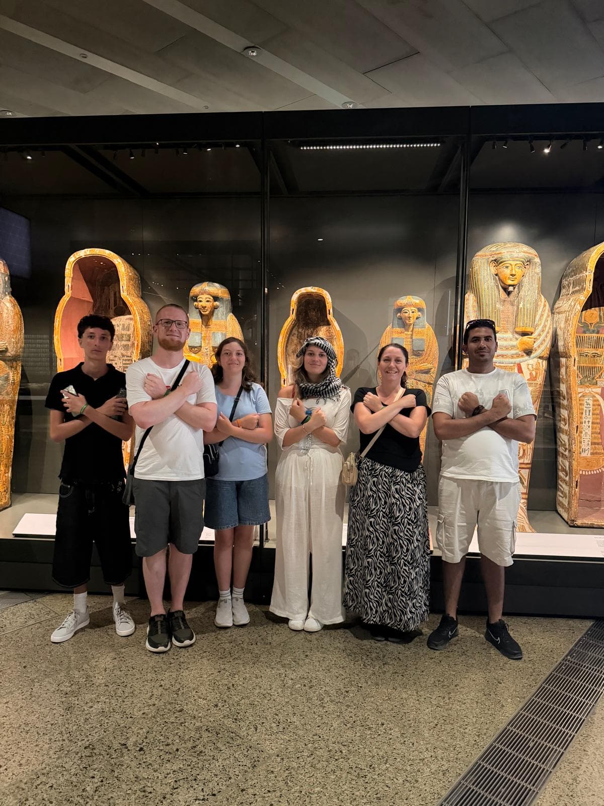 Six people pose with arms crossed in front of ancient Egyptian sarcophagi in a museum.